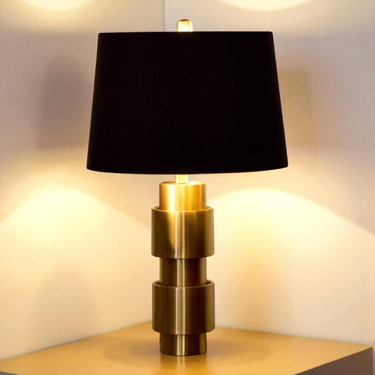 Table lamp with black shade and gold base on a wooden surface.