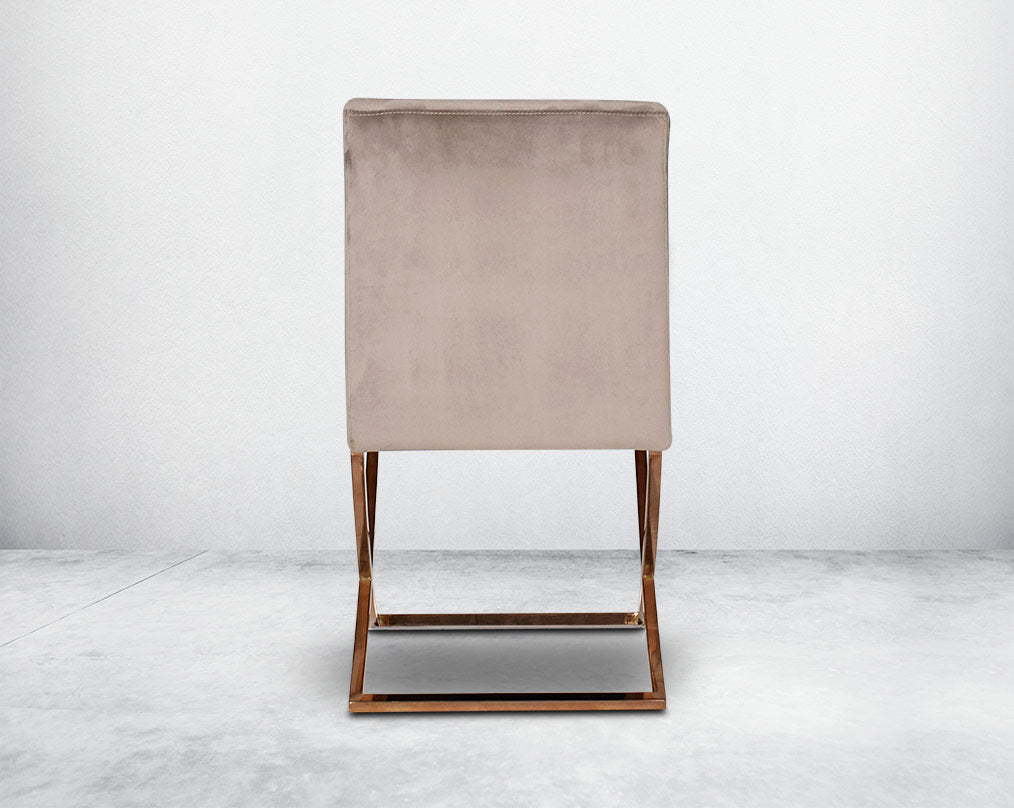 Dining chair back  upholstered in fabric with rose gold plated stainless steel legs in a cross design.