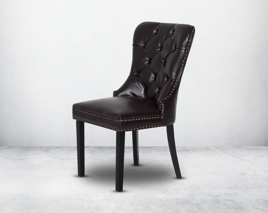 Dining chair upholstered in faux leather with buttoned tufted back the chair has antique gold rivets, legs in dark vintage brown wood.