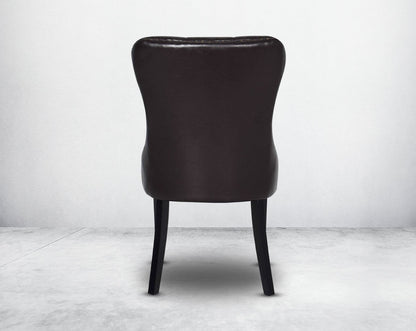 Dining chair upholstered in faux leather with back view buttoned tufted back the chair has antique gold rivets, legs in dark vintage brown wood.