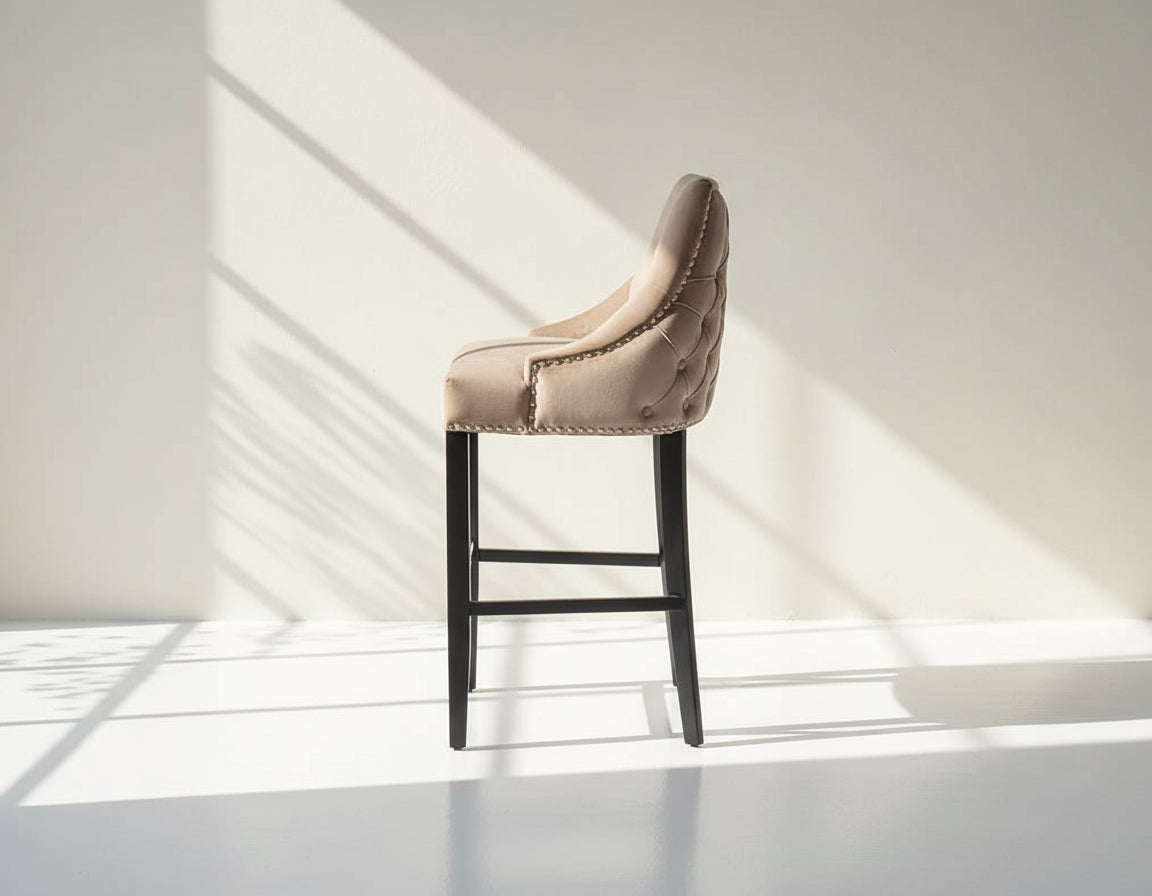 Bar chair upholstered in fabric with buttoned tufted back and silver rivets, the stool has a stainless steel front bar as a foot rest with legs in dark vintage brown wood side view 