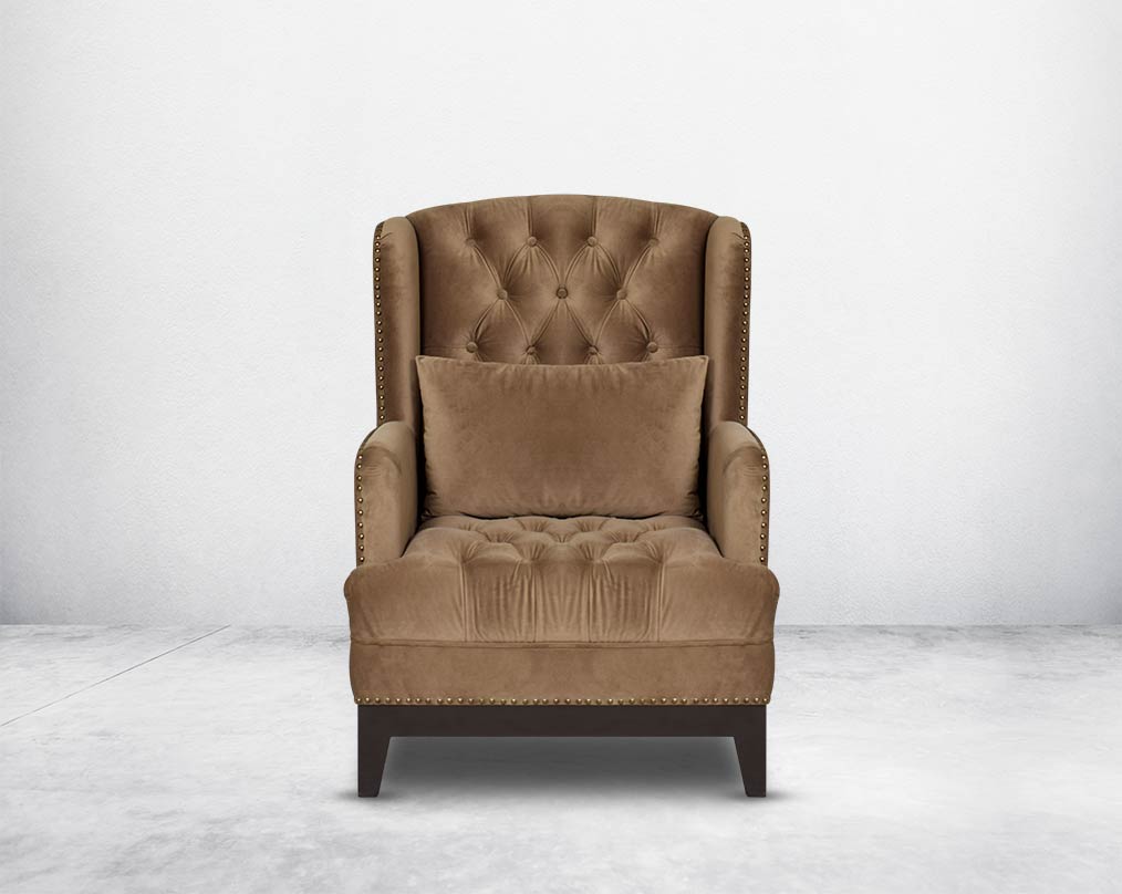 Wing arm chair upholstered in fabric and tufted with antique gold rivets on the arms and front with cushion and legs in brown oak front view