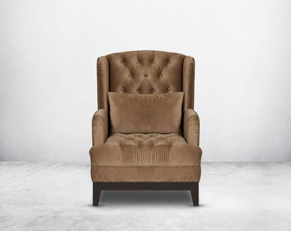 Wing arm chair upholstered in fabric and tufted with antique gold rivets on the arms and front with cushion and legs in brown oak front view