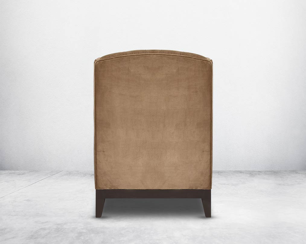 Wing arm chair upholstered in fabric and tufted with antique gold rivets on the arms and front with cushion and legs in brown oak back view