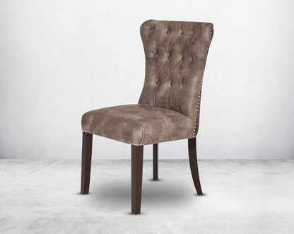 Dining chair upholstered in fabric with tufted back and birchwood legs. Stainless steel decorative ring at the back with stainless steel rivets on the sides.