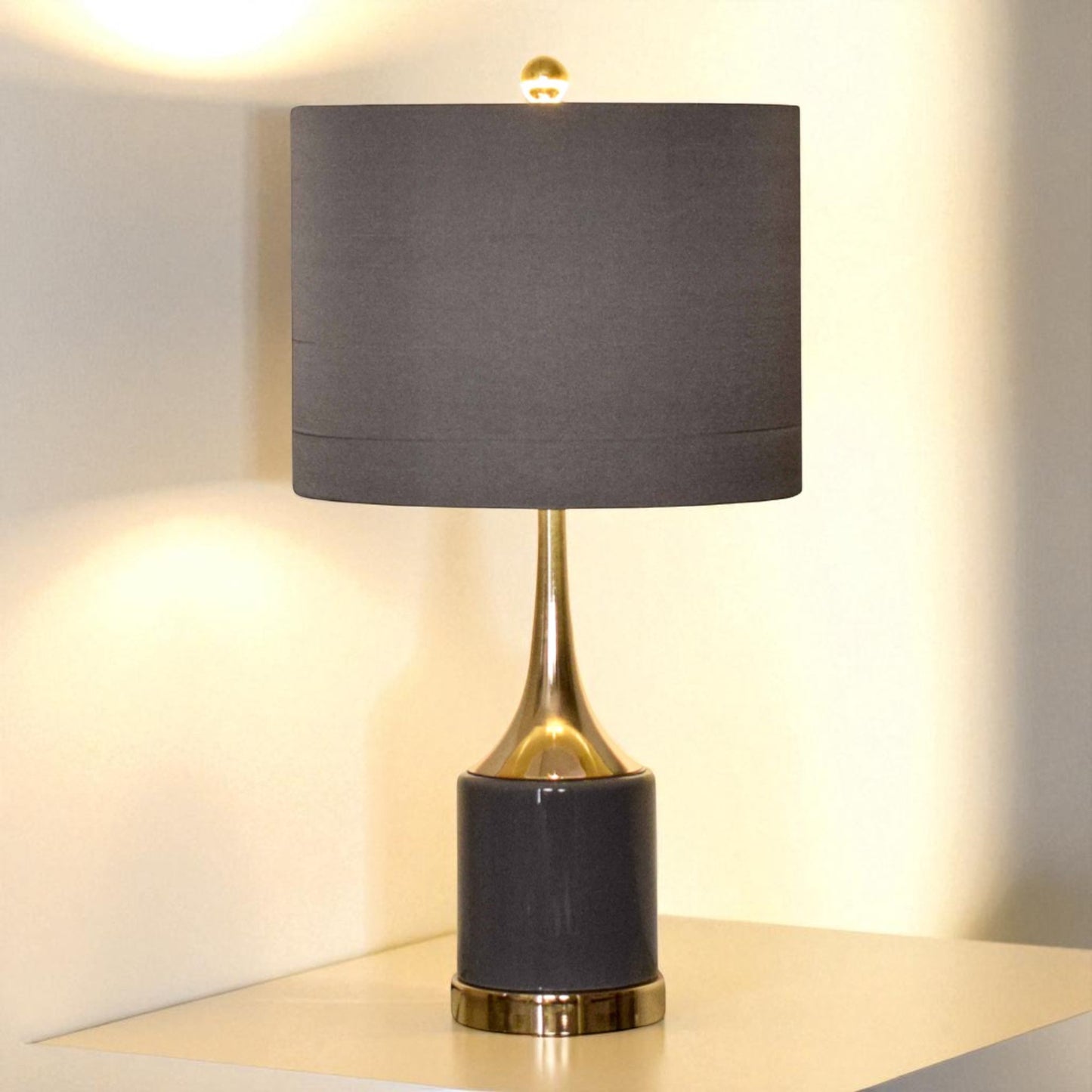 Table lamp with a dark gray shade and black base with gold accents on a light surface.