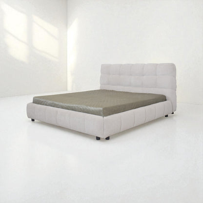 Gray upholstered bed in a minimalistic room with white walls and floor.