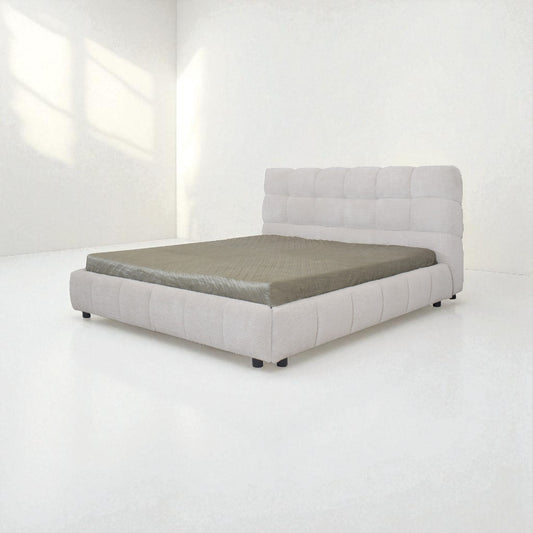 Gray upholstered bed in a minimalistic room with white walls and floor.
