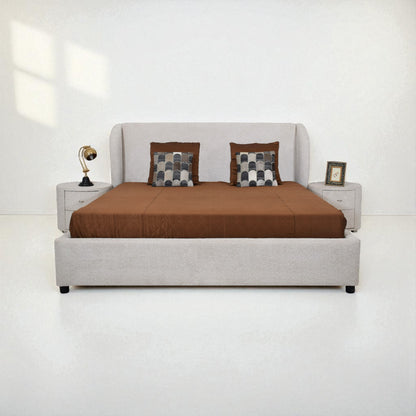 Gray upholstered bed with brown bedding and checkered pillows on a white background