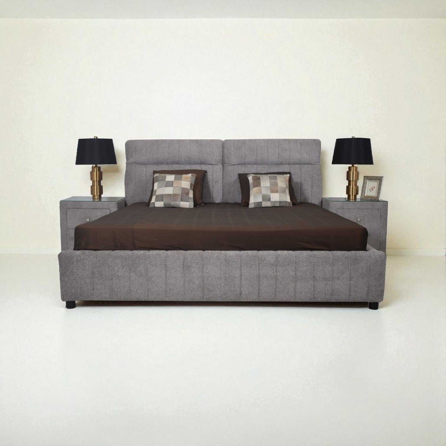 Gray upholstered bed with brown bedding and two lamps on a white background