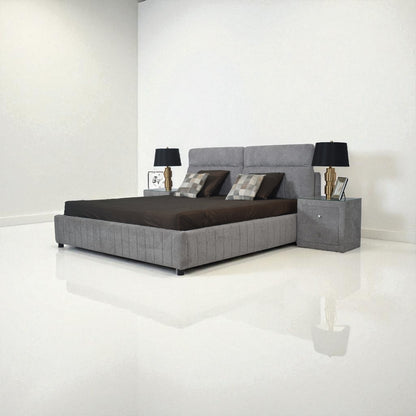 Gray upholstered bed with dark bedding in a minimalistic room.