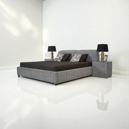 Gray upholstered bed with dark bedding in a minimalistic room.