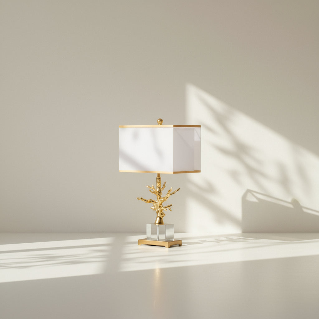 Decorative table lamp with gold branch design and white shade on a neutral background